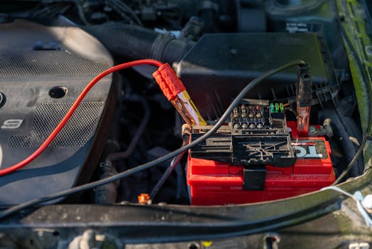 Close-up of a car battery with attached jumper cables in an engine bay.